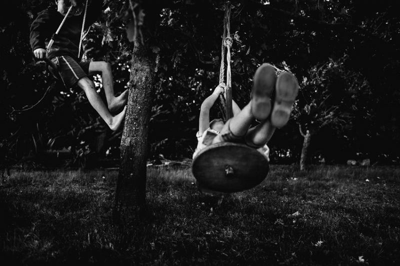 Nici Boon Tellerschaukel Zwei Kinder schaukeln unter einem Baum