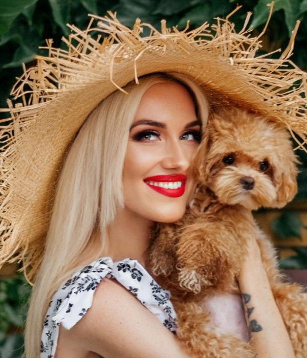 Lächelnde Frau mit Sonnenhut, die einen Schoßhund hält