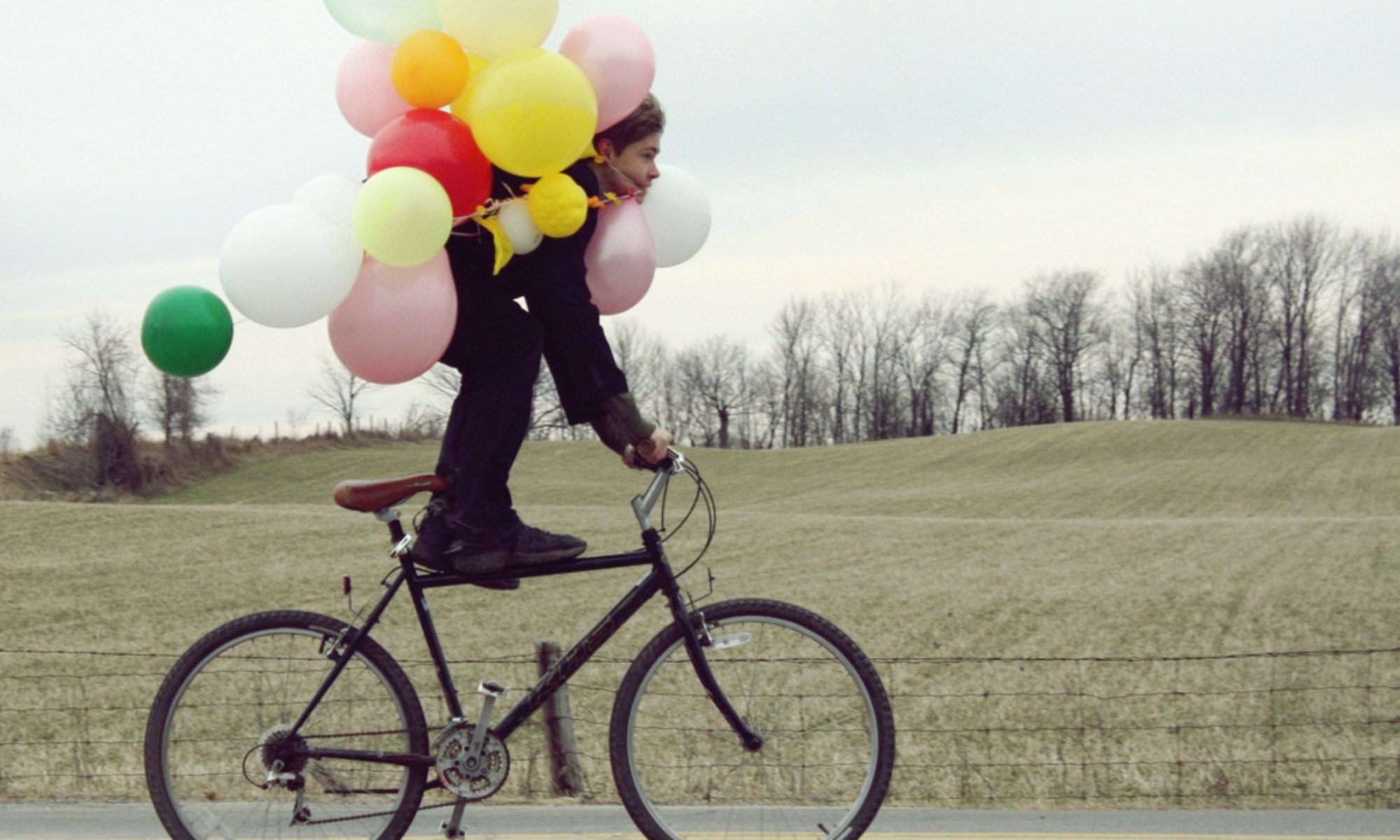 Junge mit Luftballons auf einem Fahrrad.