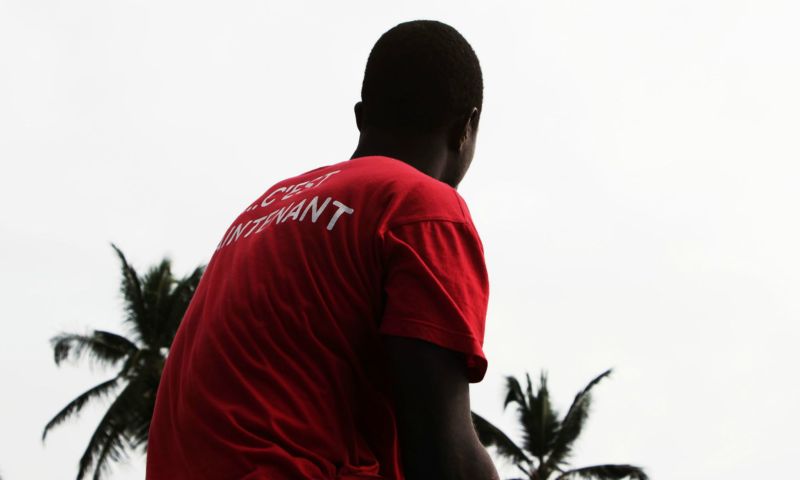 yannis guiba Afrikanischer Mann mit rozem Shirt vor Palmen