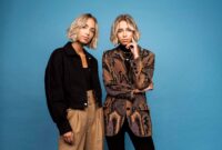 Die beiden blonden Zwillinge Lisa und Lena stehen vor einer blauen Wand und schauen in die Kamera