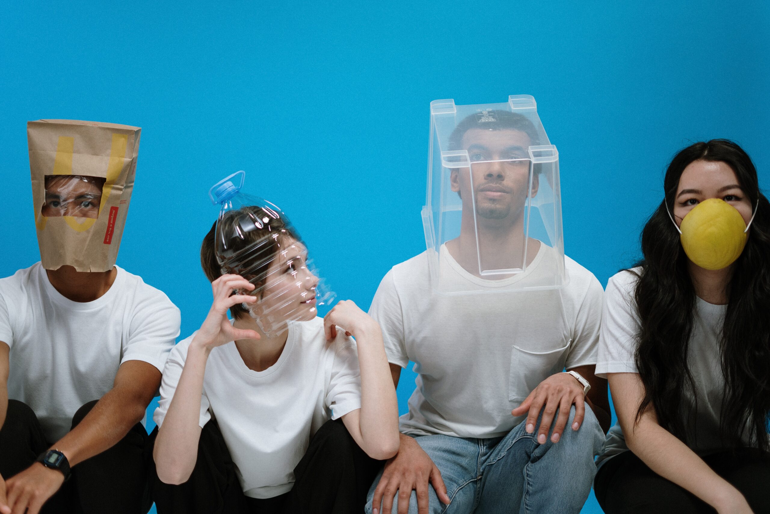 Vier junge Menschen tragen Corona-Masken aus seltsamen Materialien, beispielsweise eine Plastikflasche, über dem Kopf