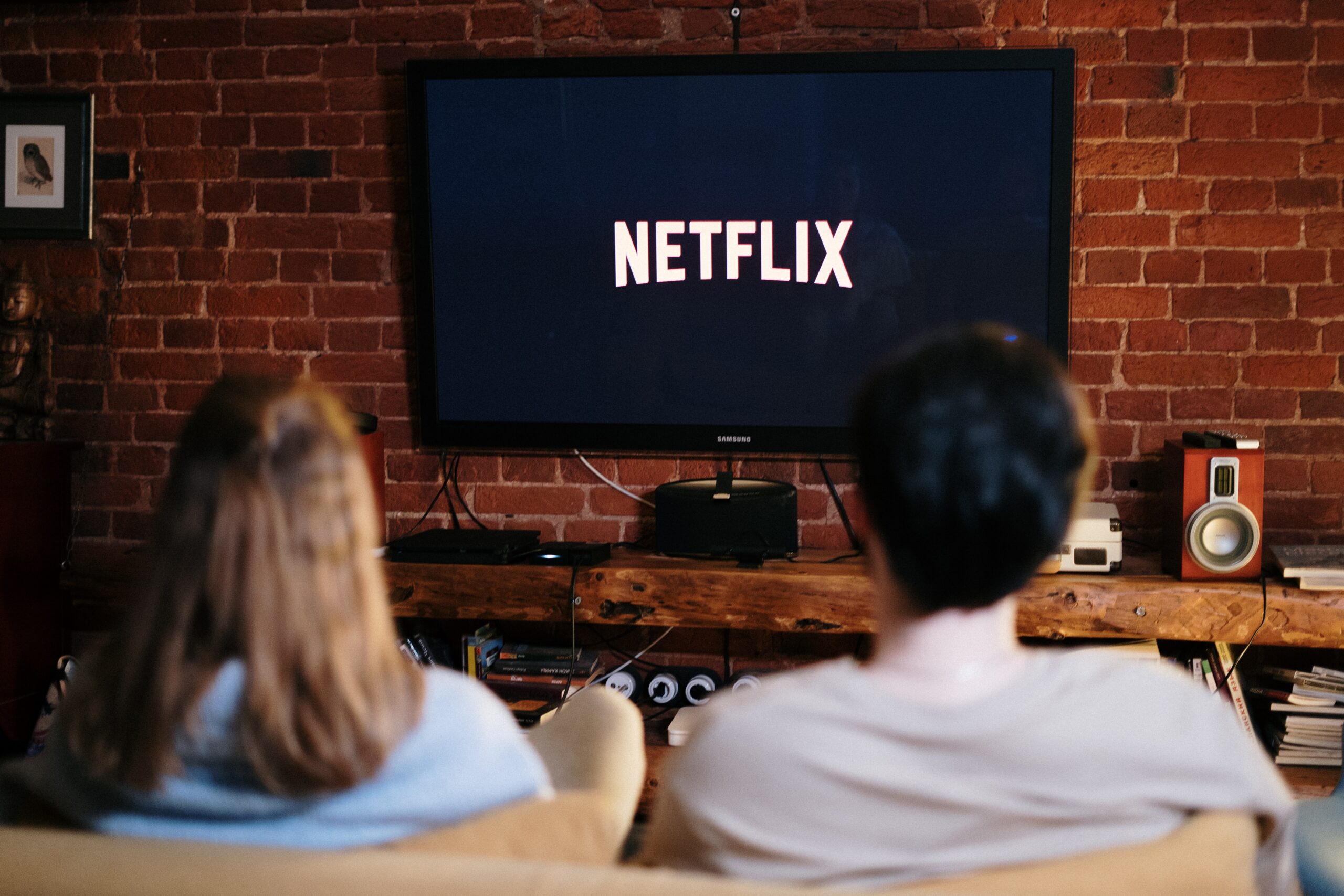 Ein Mann und eine Frau sitzen mit dem Rücken zur Kamera auf einem Sofa, auf ihrem Fernseher läuft Netflix