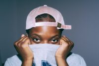 eine junge Frau mit grauem Shirt und rosafarbener Cap bedeckt ihren Mund mit ihrem Shirt und schaut peinlich berührt