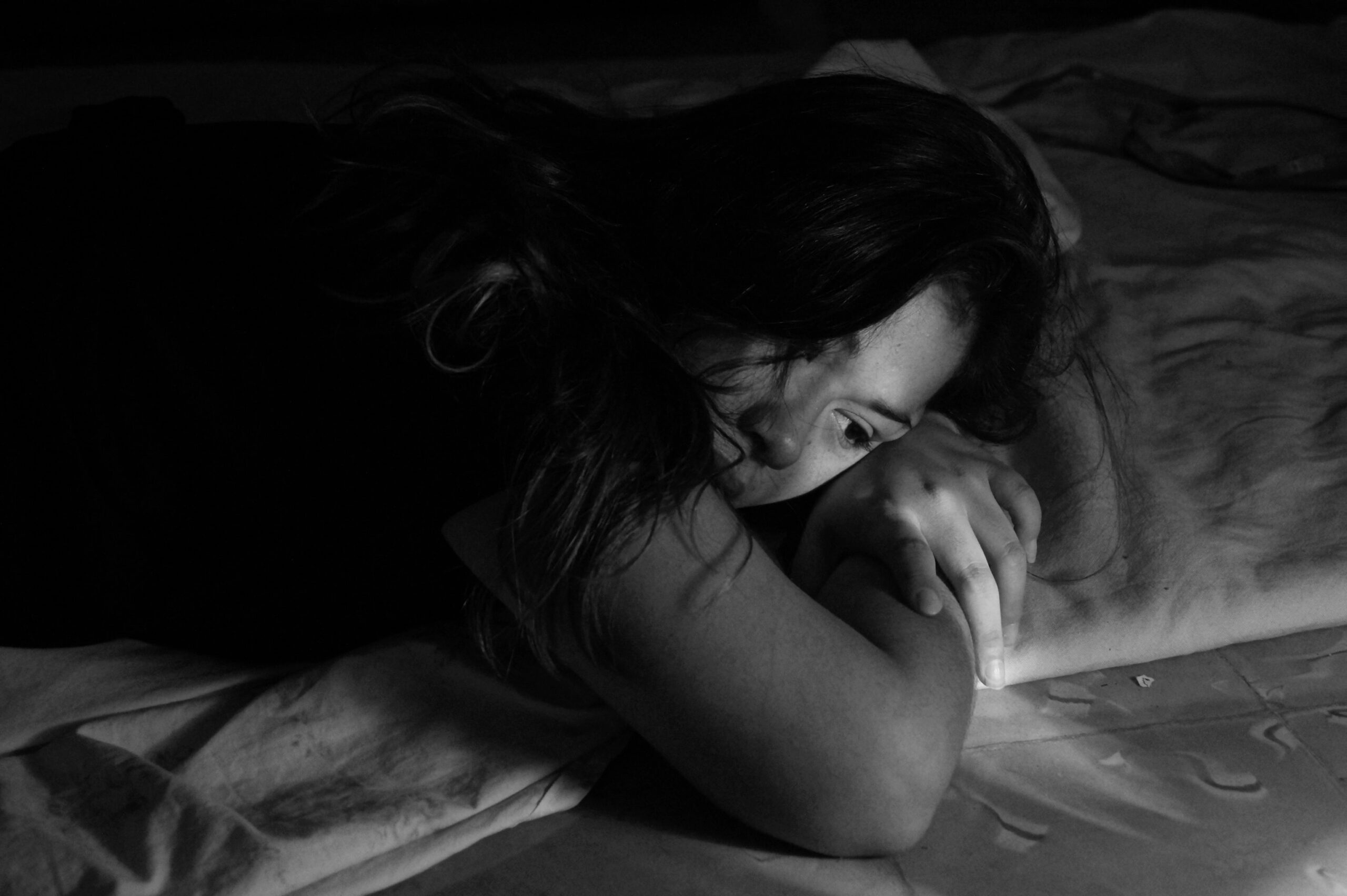 Eine Frau liegt im Bett und schaut traurig. Das Foto ist schwarz-weiß.