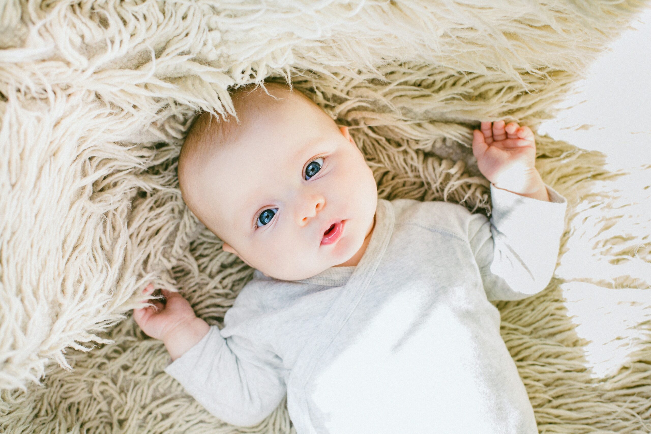 Ein Baby liegt auf einer Decke und schaut in die Kamera