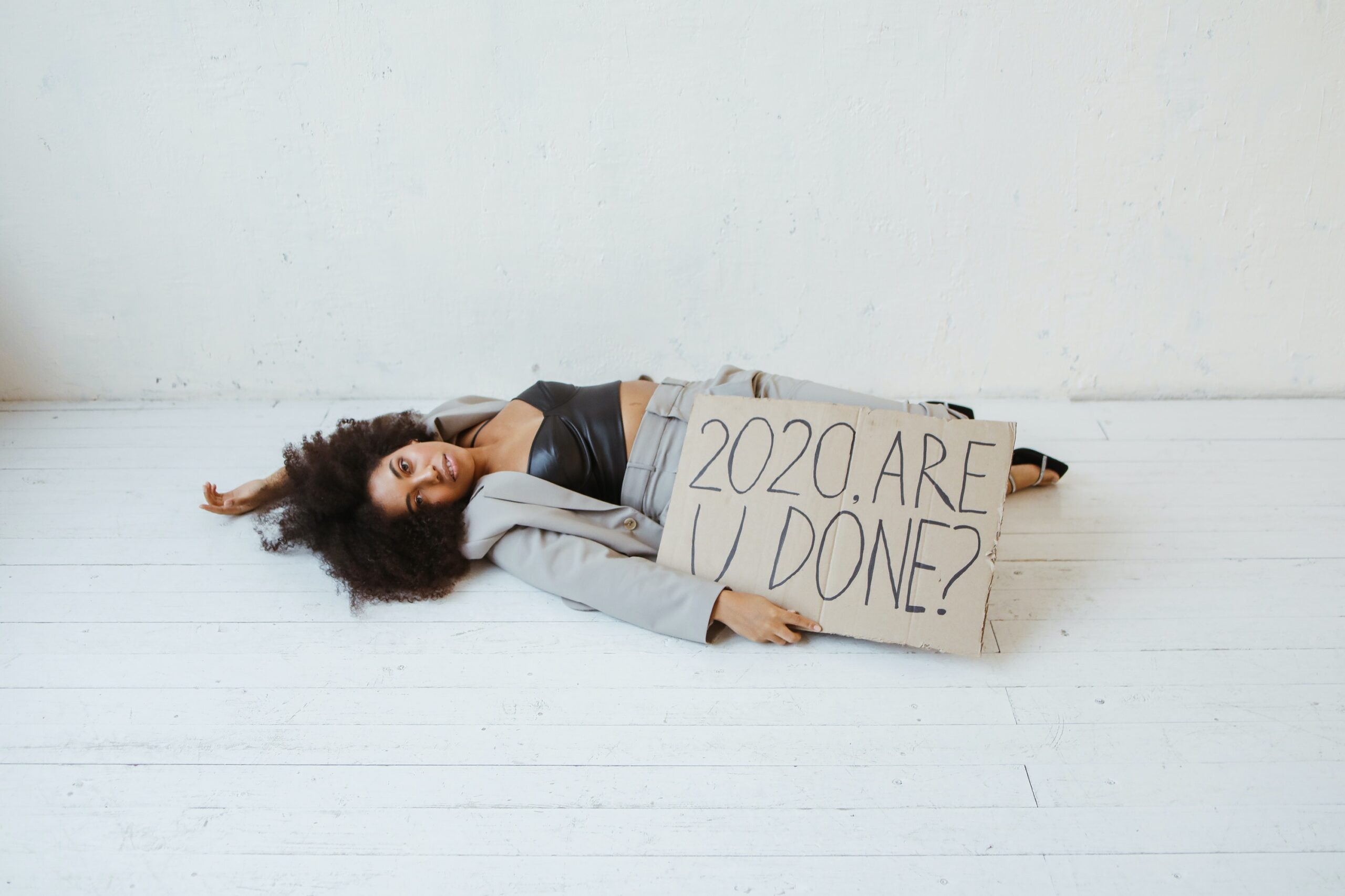Eine Frau liegt auf dem Boden. Sie hält ein Schild in der Hand, auf dem "2020 are you done?" steht.