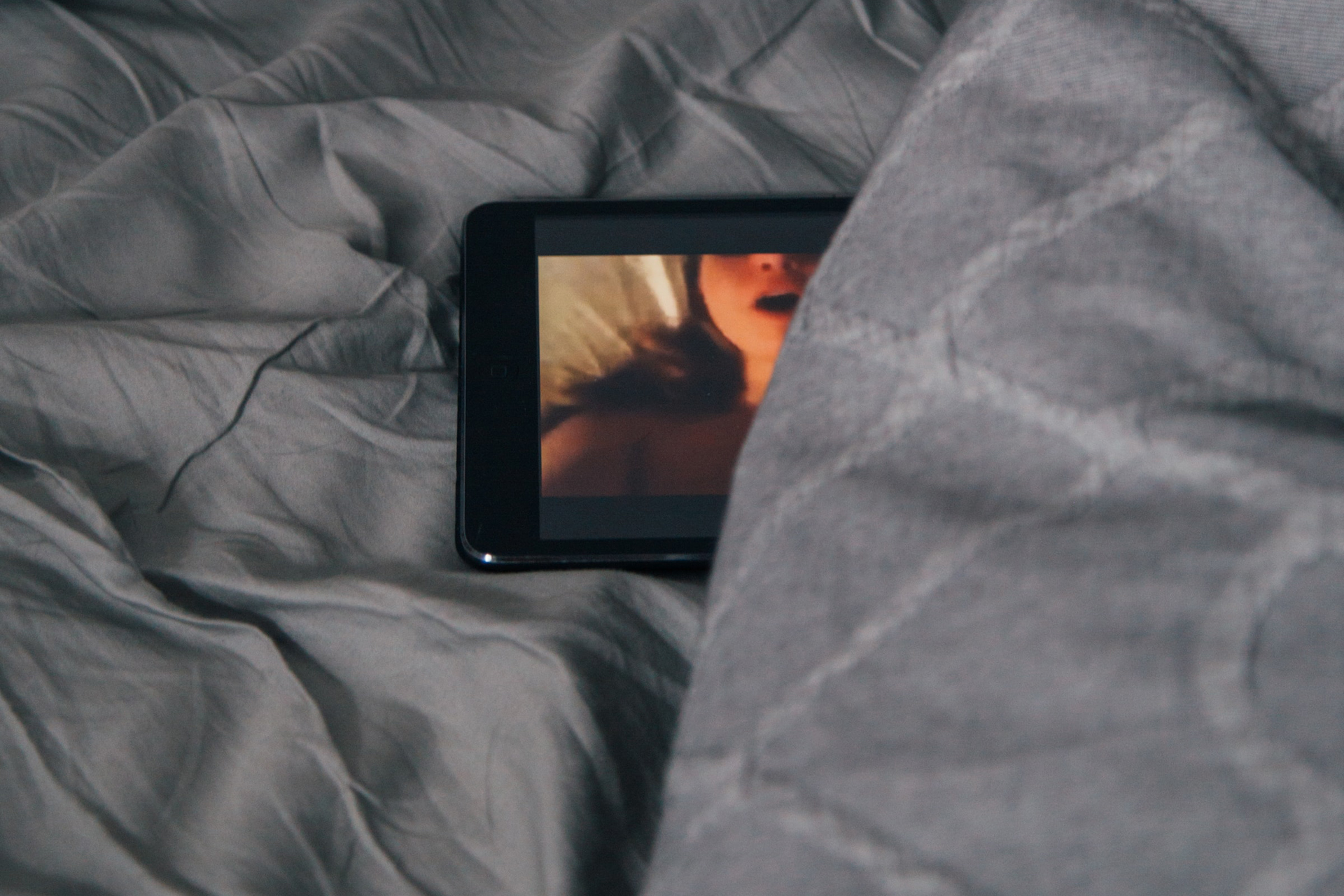 Smartphone liegt im Bett und zeigt einen Porno