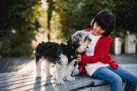 Ein Junge sitzt neben einem Hund und streichelt ihn