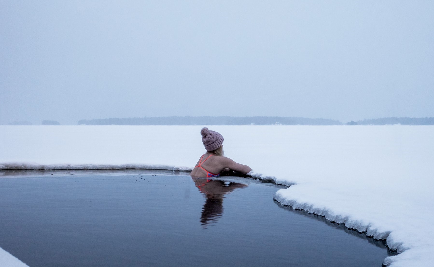 Frau mit Mütze im Wasser umgeben von Schnee