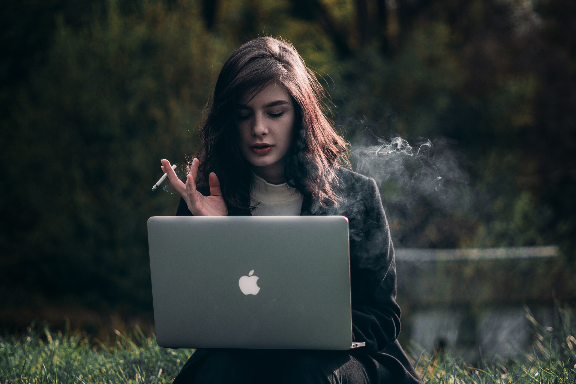 Eine Frau sitzt mit einem Laptop im Gras und raucht