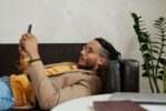 Mann liegt mit Smartphone auf dem Sofa