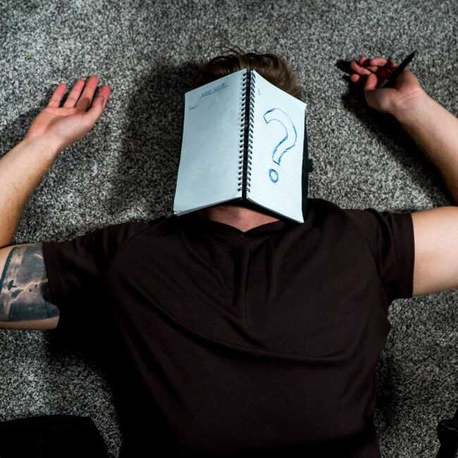 Mann liegt auf dem Boden mit einem Schreibheft über dem Gesicht