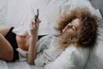 Frau liegt mit Smartphone im Bett