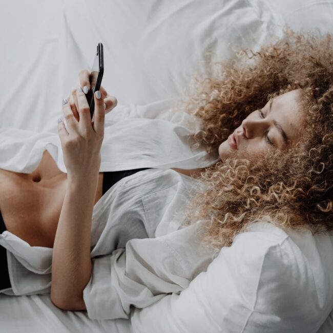 Frau liegt mit Smartphone im Bett