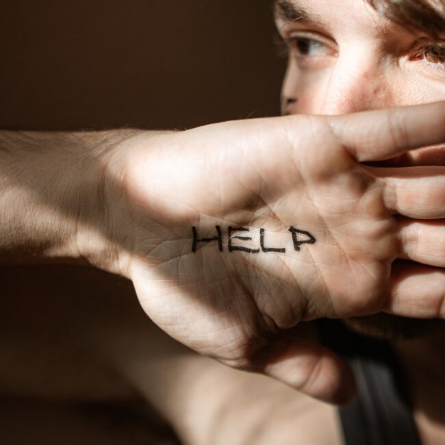 Mann der seine Hand mit der Aufschrift "Help" vors Gesicht hält