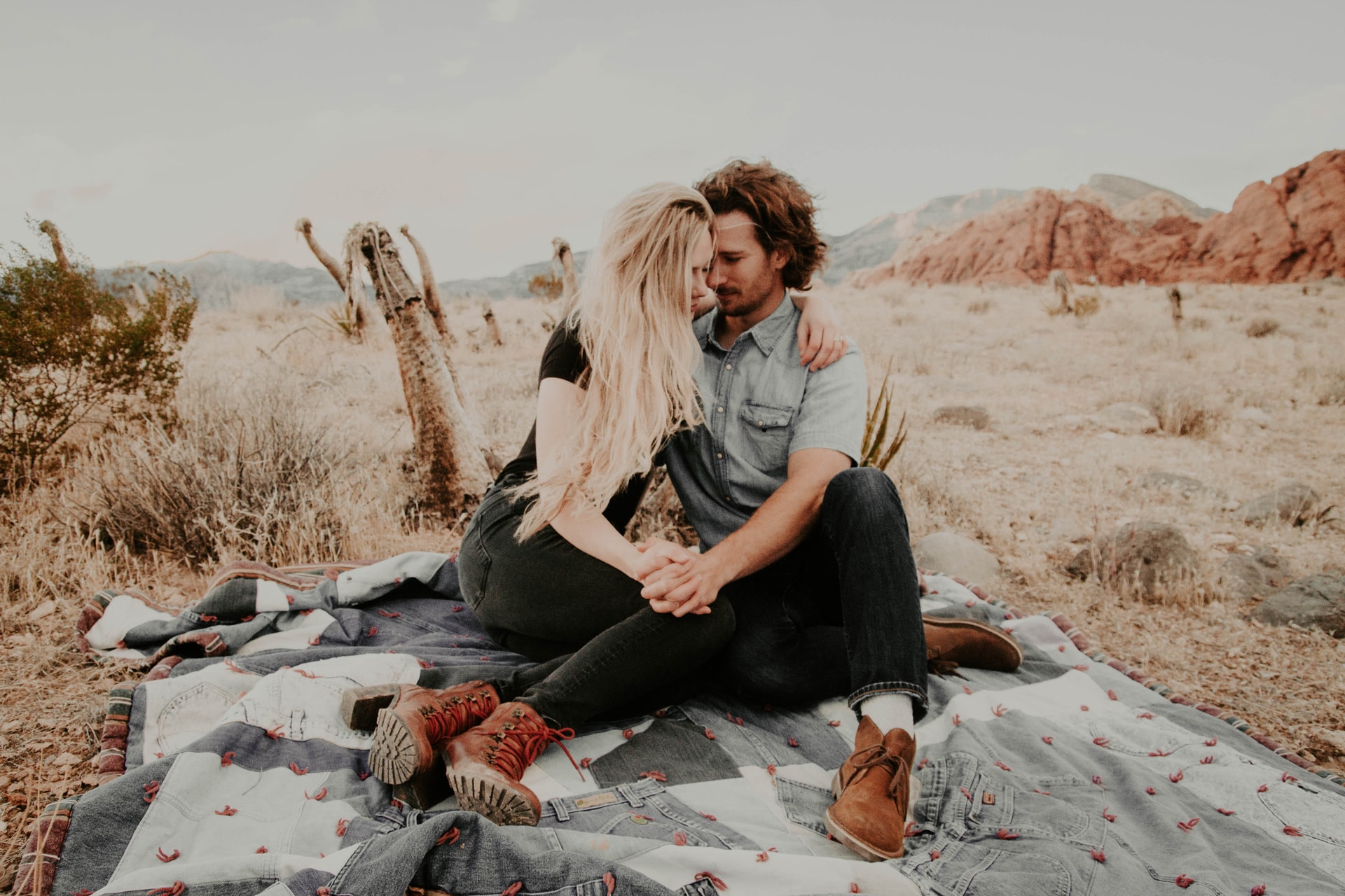 Mann und Frau sitzen draußen auf einer Decke und halten Händchen