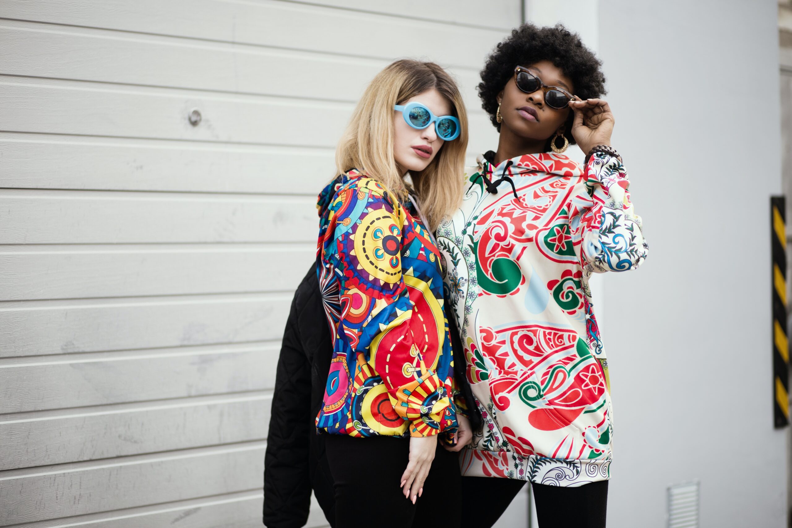Zwei Frauen posieren in bunten Klamotten vor einer Mauer