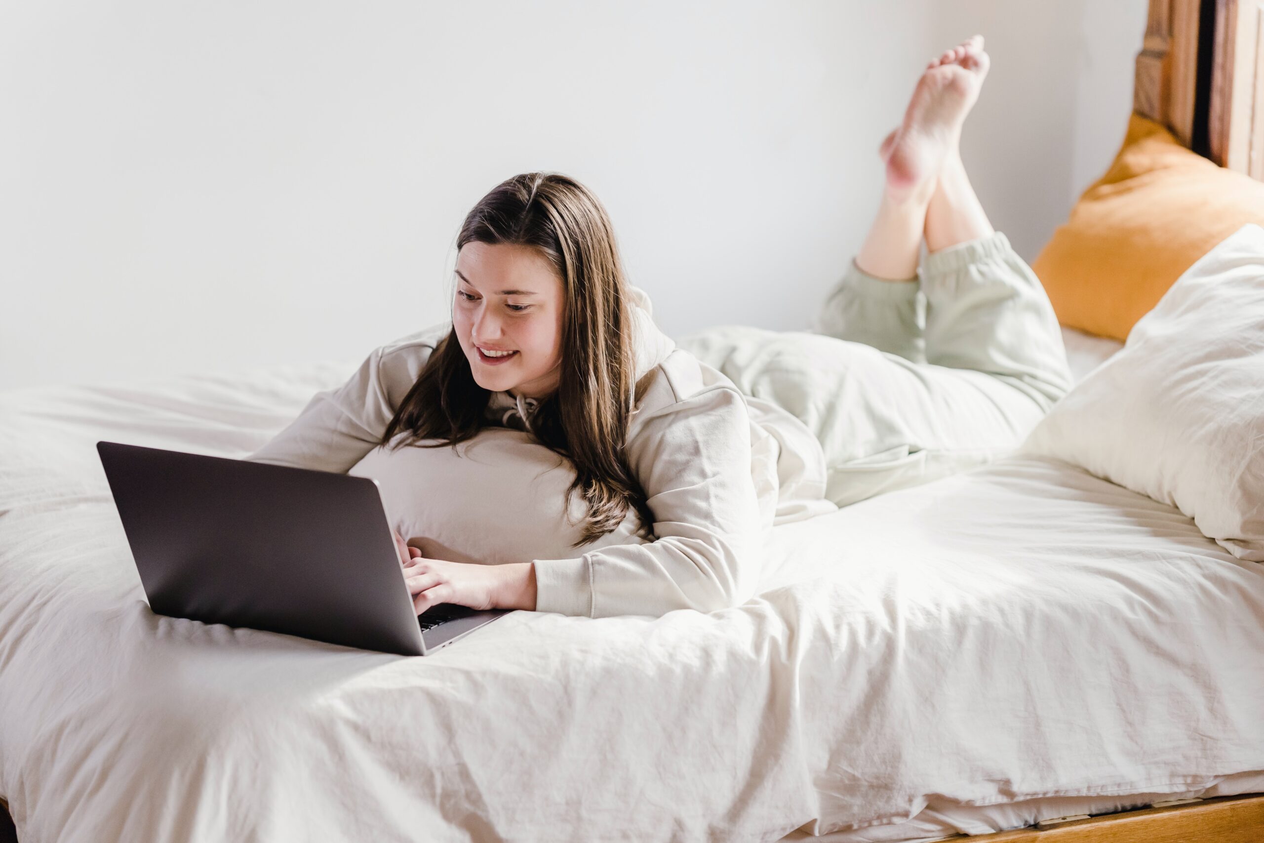 Eine junge Frau liegt im Trainingsanzug auf dem Bett und schaut auf einen Laptop