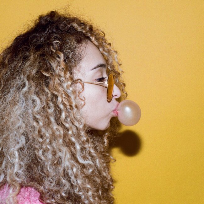 Eine Frau mit Sonnenbrille macht eine Kaugummiblase