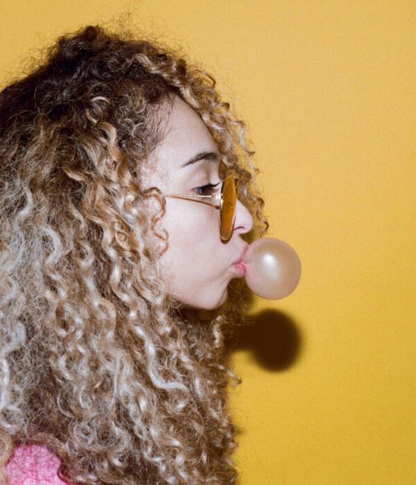 Eine Frau mit Sonnenbrille macht eine Kaugummiblase