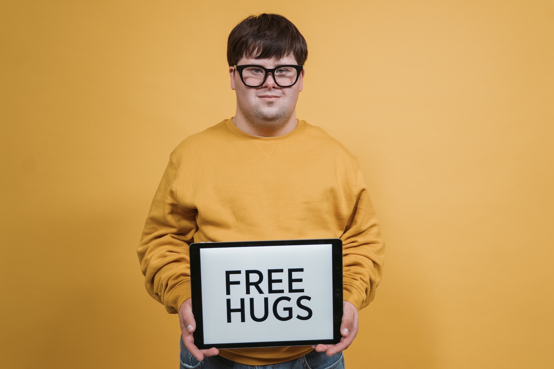 Ein Mann mit Down-Syndrom hält ein Schild mit der Aufschrift: „FREE HUGS".
