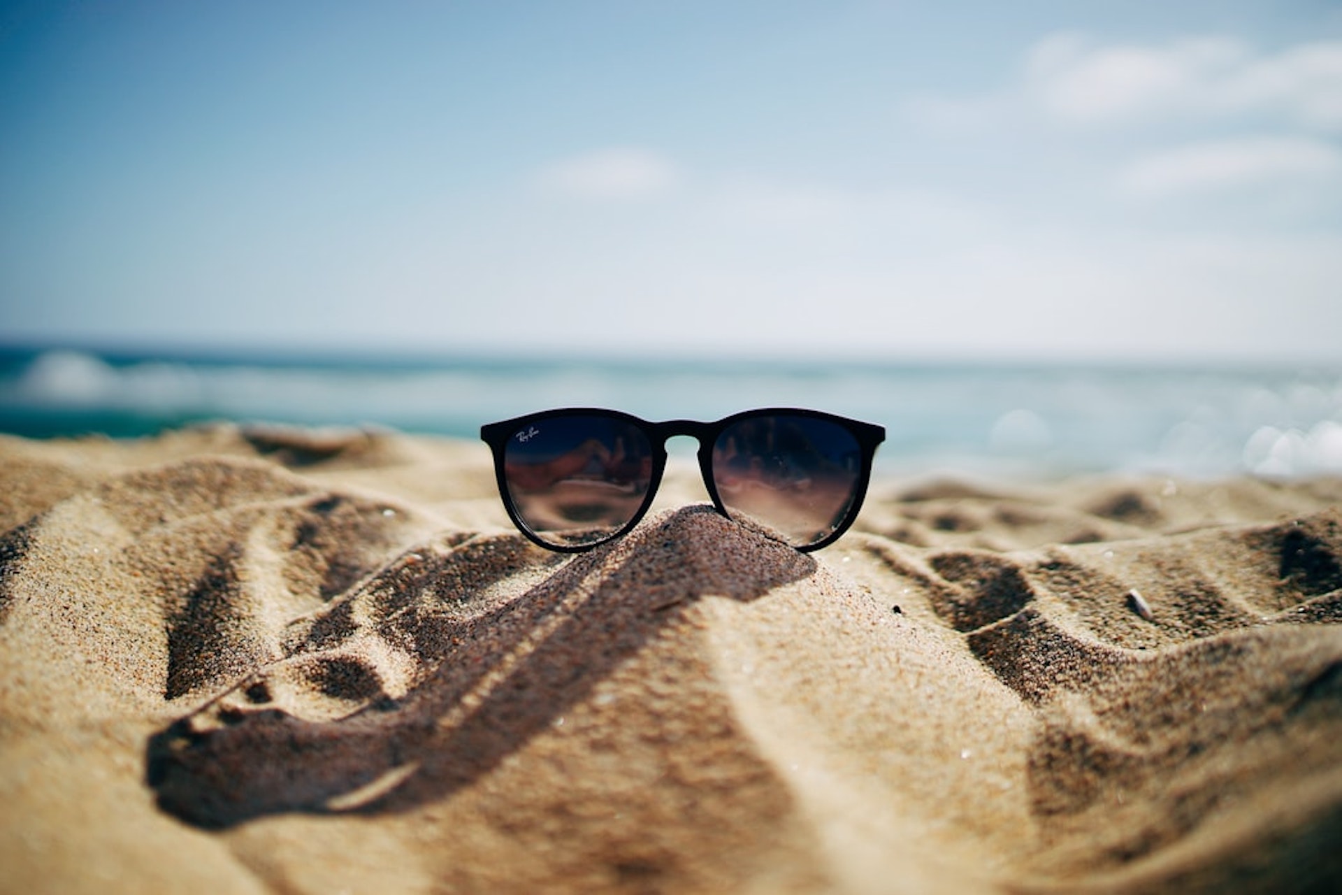 Ein Sandhügel auf dem eine Sonnenbrille liegt.