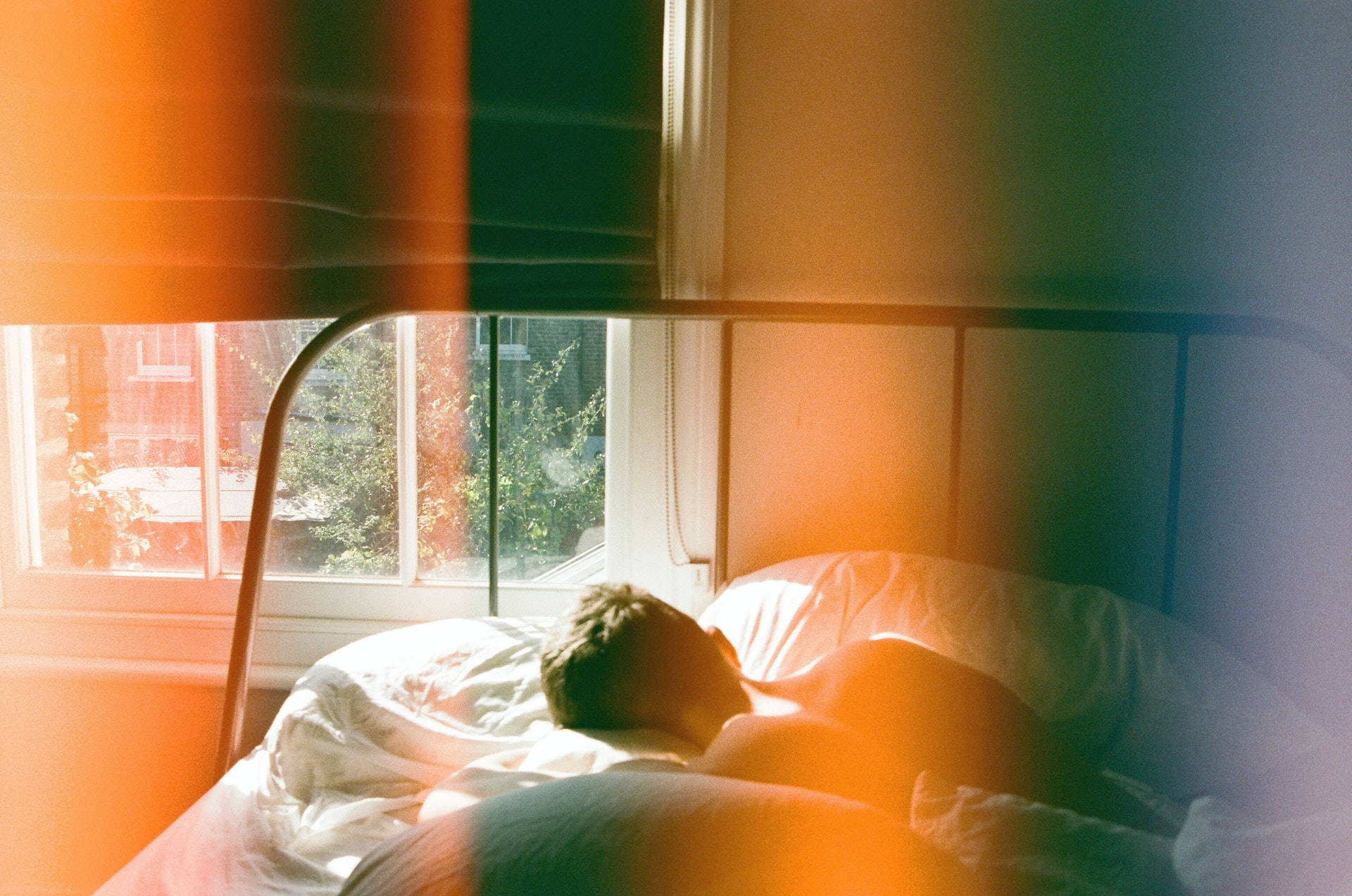 Mann liegt auf einem Bett zu einem offenen Fenster gerichtet