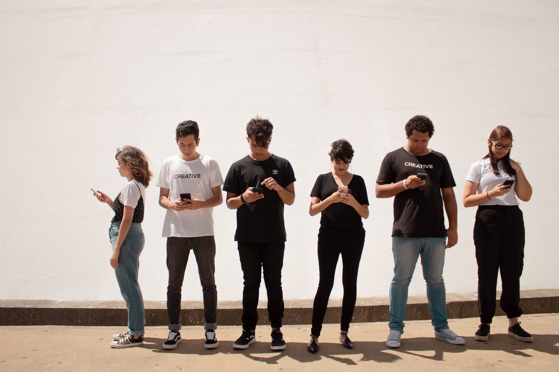Eine Gruppe von Jugendlichen stehen in einer Reihe und schauen auf das jeweilige Smartphone.
