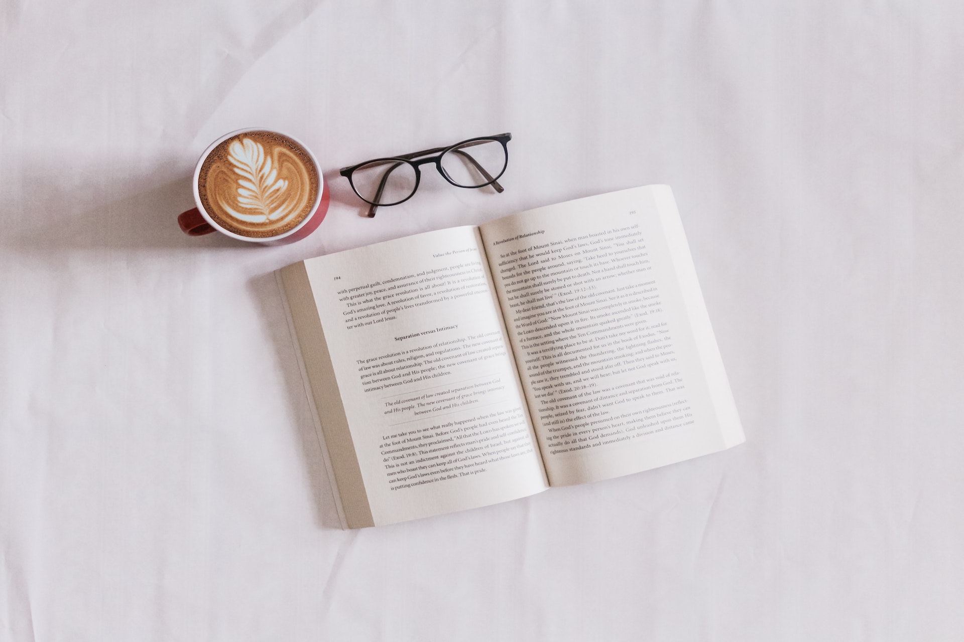 Ein Buch, eine Kaffeetasse und eine Brille liegen auf einem Bett.