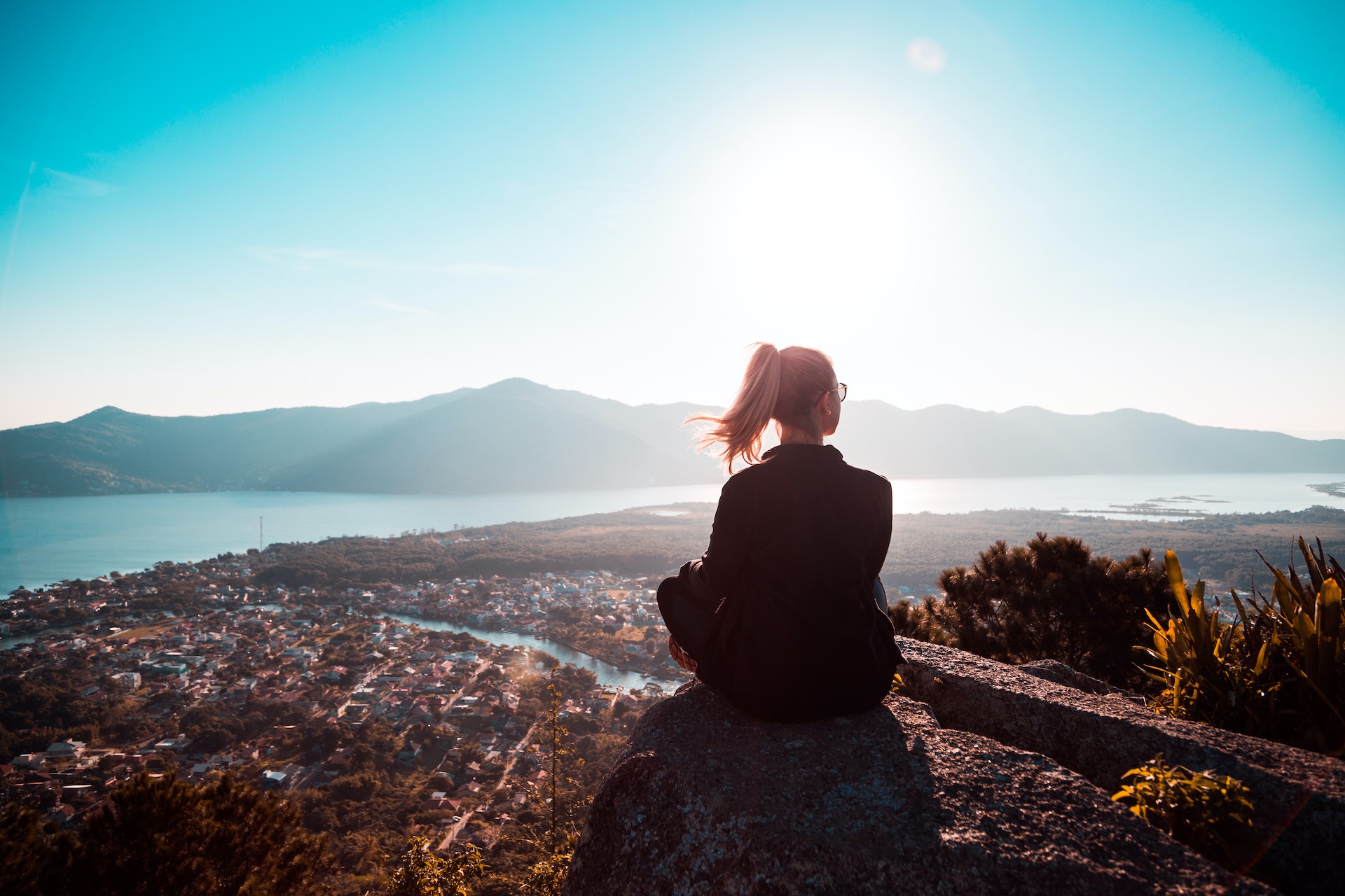 Eine Frau sitzt auf einem Berg und schaut in den Himmel. Bild: Pexels