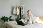 Frau sitzt mit Laptop auf Bett. Bild: Pexels