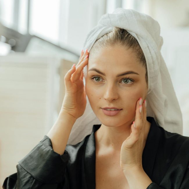 Eine Frau mit Handtuch um den Kopf sieht sich im Spiegel an