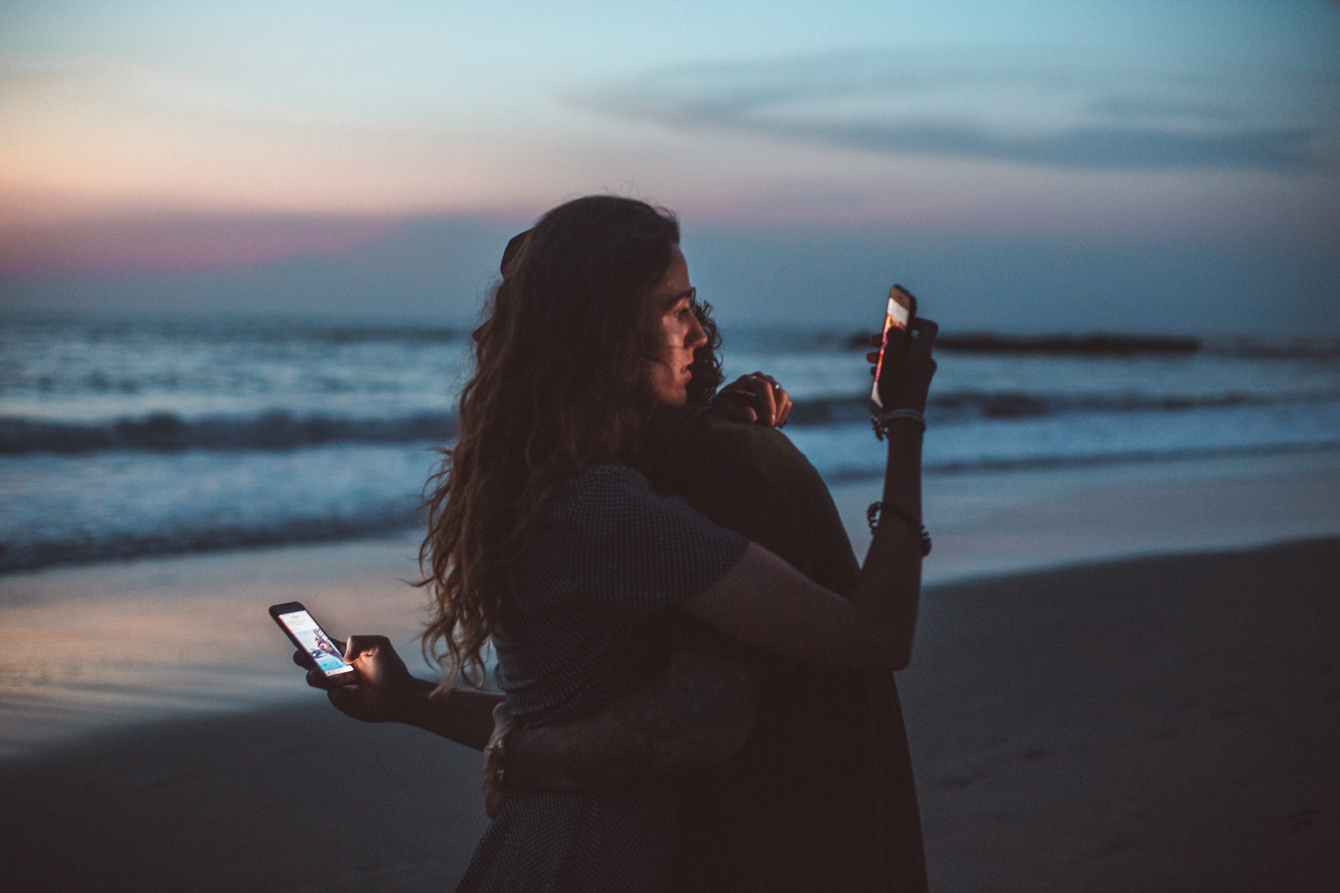 Zwei Personen umarmen sich und halten dabei jeweils ein Handy in der Hand.