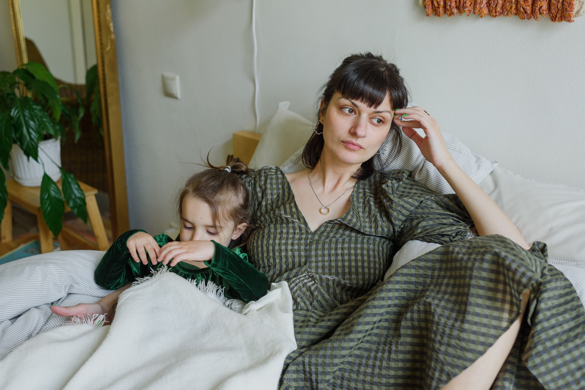 Eine Mutter sitzt mit ihrem Kind auf einem Bett und guckt traurig zur Seite. Bild: Pexels