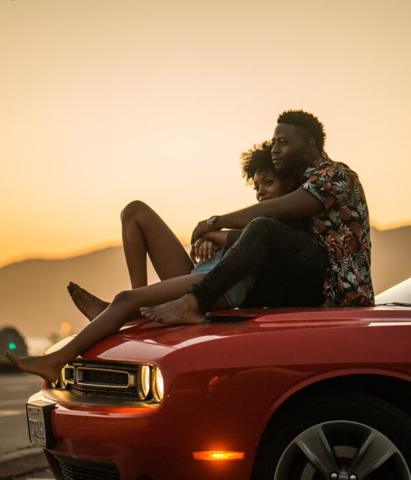 Frau und Mann sitzen auf der Motorhaube eines Autos