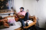 Mann sitzt mit Ukulele auf seinem Bett