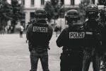 zwei Polizisten in Uniform von hinten, ein dritter Polizist sieht in die Kamera