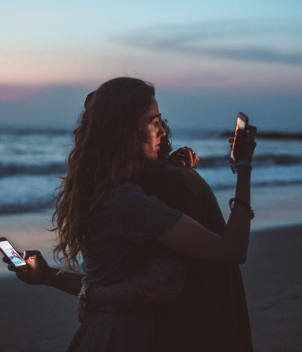 Zwei Menschen umarmen sich und schauen auf ihre Handys dabei